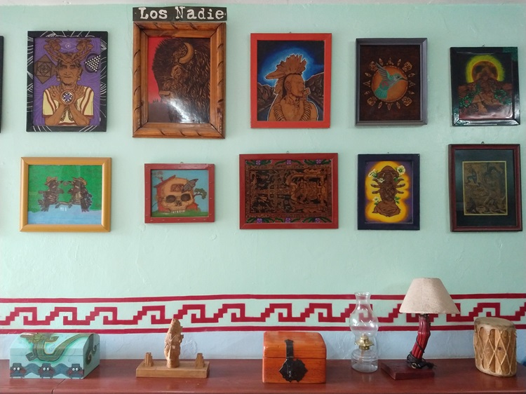Cuadros cuelgan de una pared y artesanías mexicanas sobre un mueble