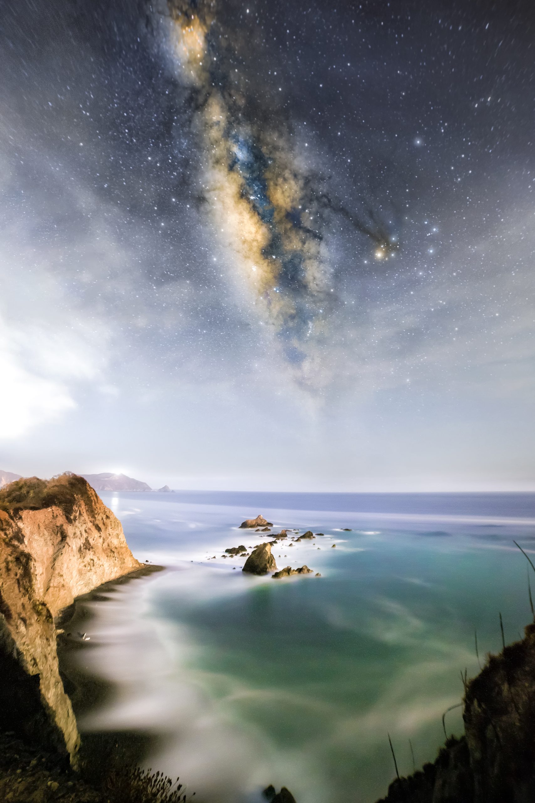 En el cielo se muestra un cúmulo de estrellas que parecen reunidas en una nebulosa que desaparece en el horizonte del mar de la Costa Sur de Jalisco, con playas rocosas de donde rompen las olas en las playas de Melaque, Jalisco.